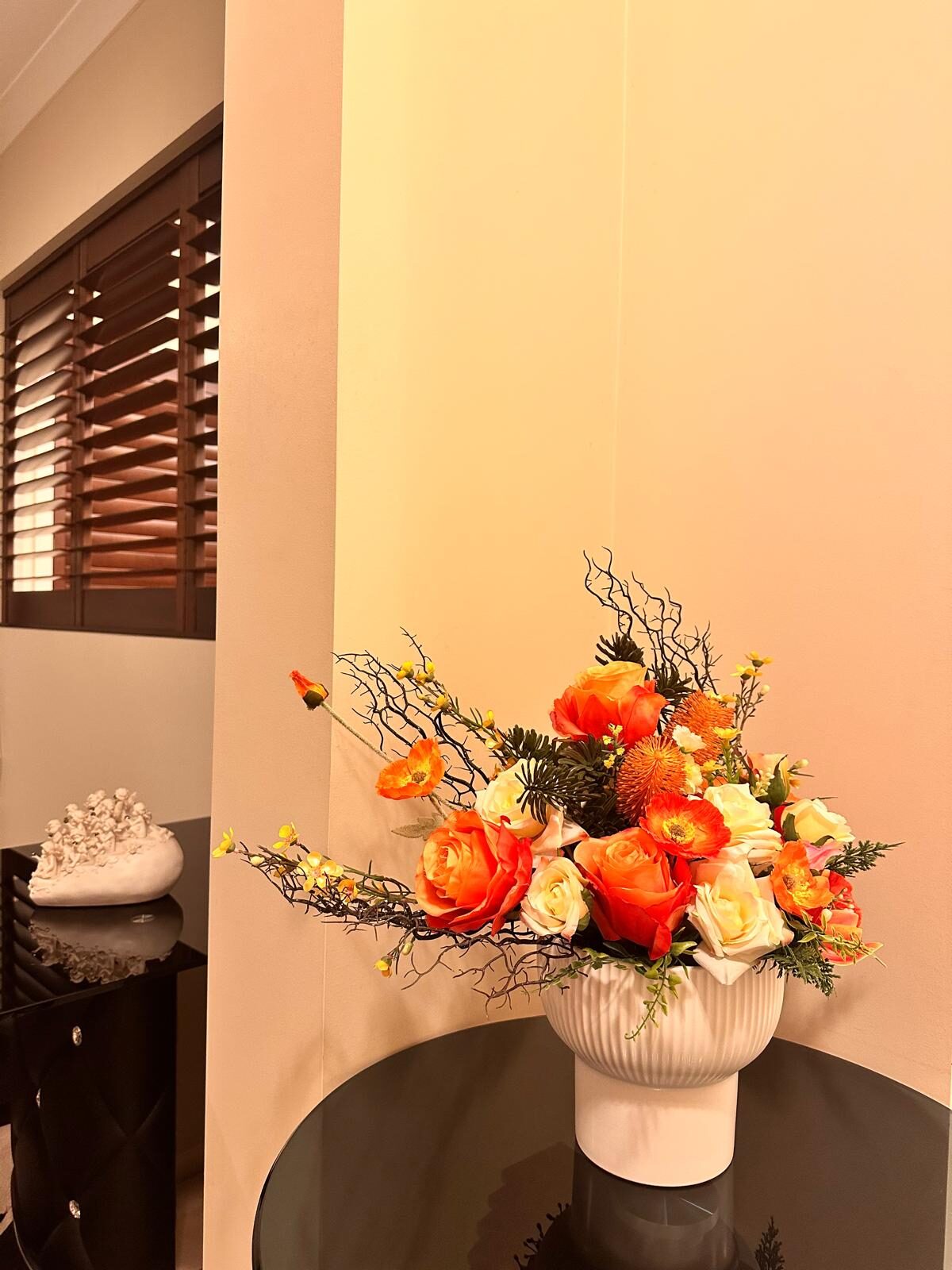 Garden-style arrangement of orange roses, cream roses and poppies with dark curly willow, styled in a white ribbed pot, by Bloom by Sindra