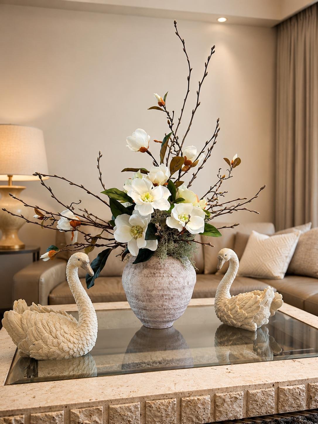 Magnolia and branch arrangement in a rustic stone-effect vase, styled with carved stone swan figurines, by Bloom by Sindra